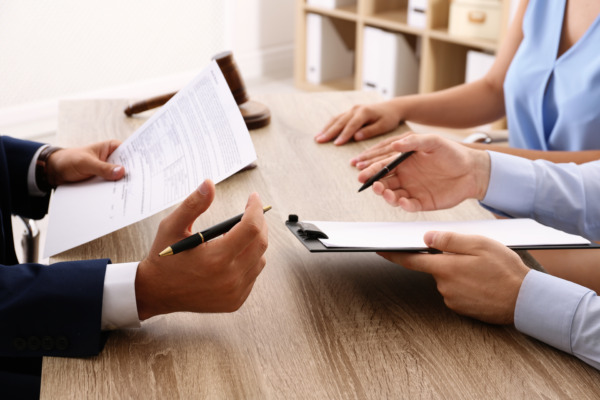 Solicitor working with clients at table in office as they discuss Power of Attorney, focus on hands