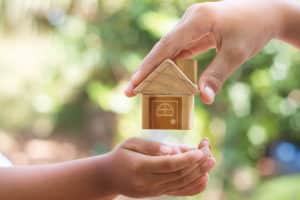 adult hand passing wooden house to child hand in article what age children should inherit in my will