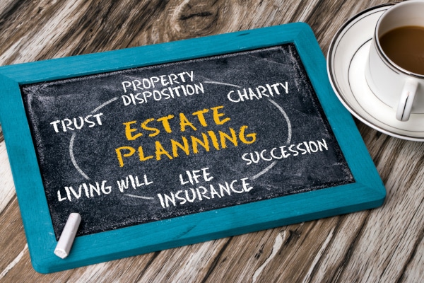 Photo of a blackboard sitting on a table beside a cup of coffee containing words and phrases explaining the importance of estate planning