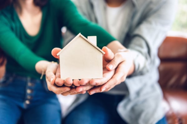 Couple holding a wooden house in their hands whilst discussing survivorship destination in Scotland