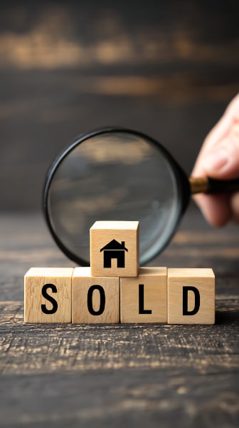 Magnifying glass behing wooden blocks spelling out the word Sold wth a drawing of a house on a block sitting on top as we discuss missives in Scotland