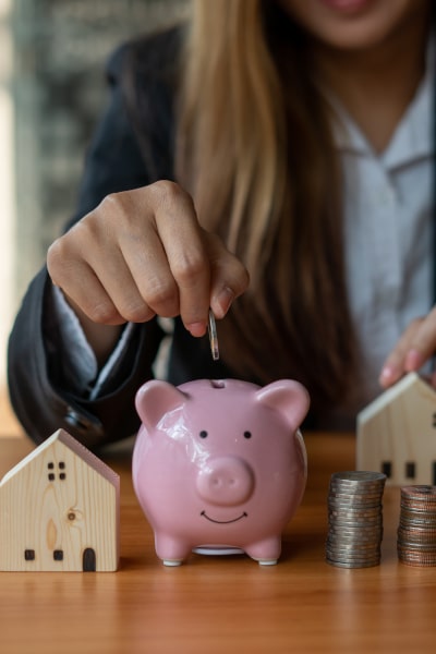Model houses and a piggy bank with a woman putting a coin into it representing a first-time buyer deposit and shared equity.